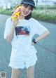 A woman in a white shirt and shorts holding a toy gun.